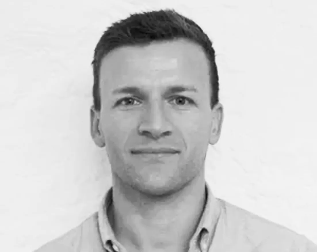 Black and white portrait of a man with short hair wearing a collared shirt, smiling slightly.