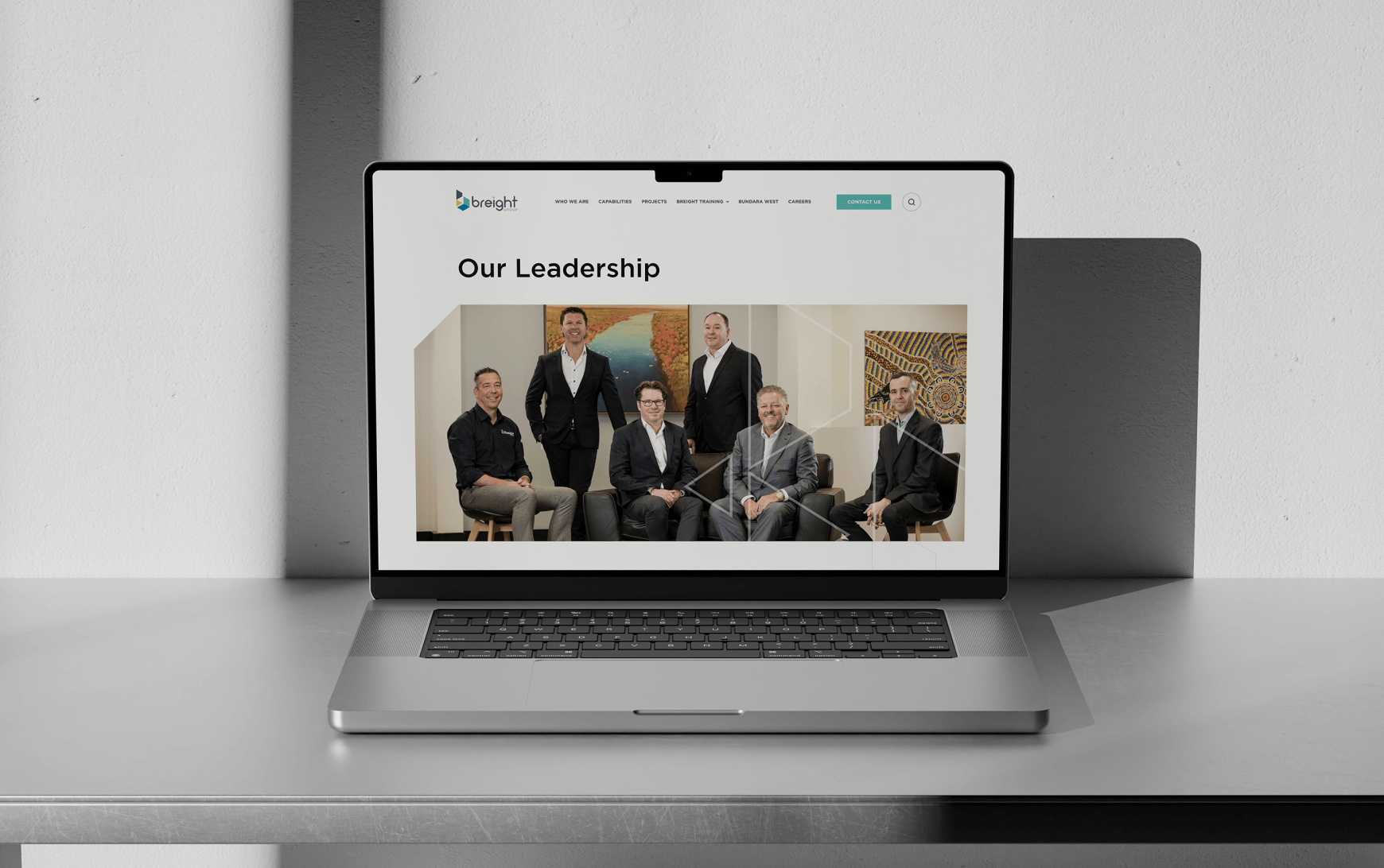 A laptop displaying a webpage titled "Our Leadership" with six men in a group photo on the screen.