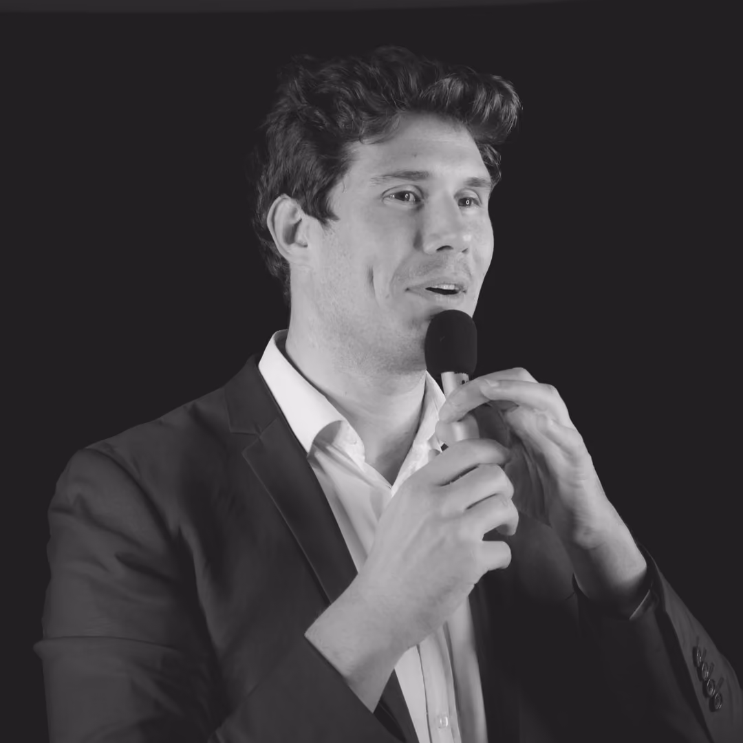 Un homme en costume parlant dans un microphone noir sur fond noir.