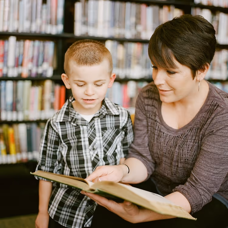Eine Frau liest gemeinsam mit einem Jungen ein Buch in einer Bibliothek.