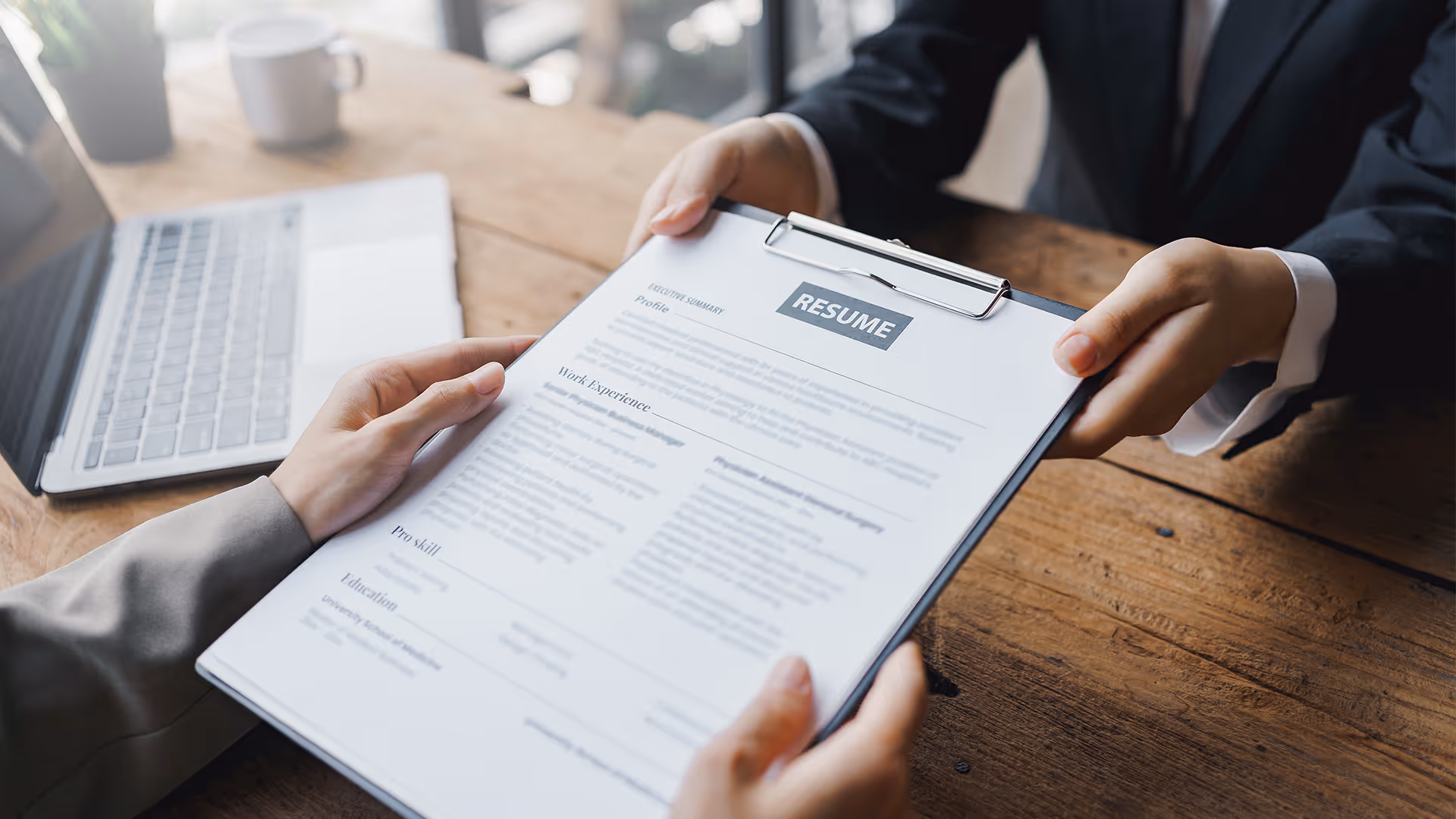 Person erhält einen Lebenslauf auf einem Klemmbrett während eines Bewerbungsgesprächs.