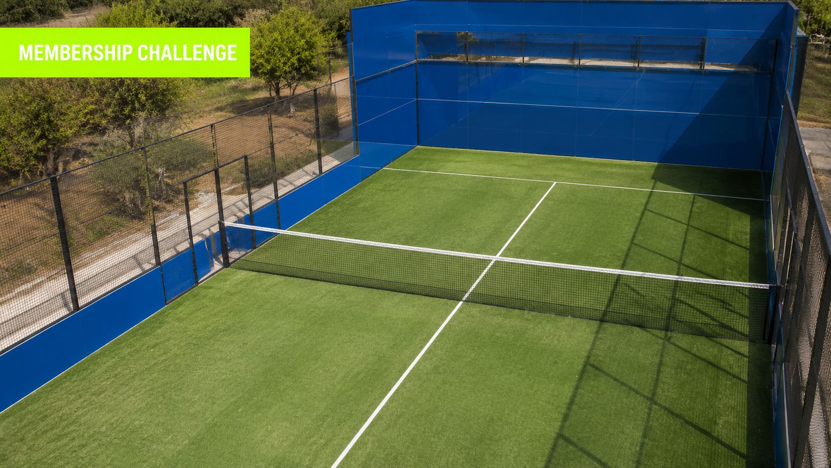 An aerial view of a professional outdoor padel court with green artificial turf and blue walls.