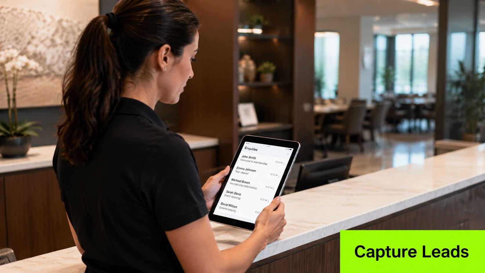 A staff member standing at a reception counter using a tablet to view client enquiries.