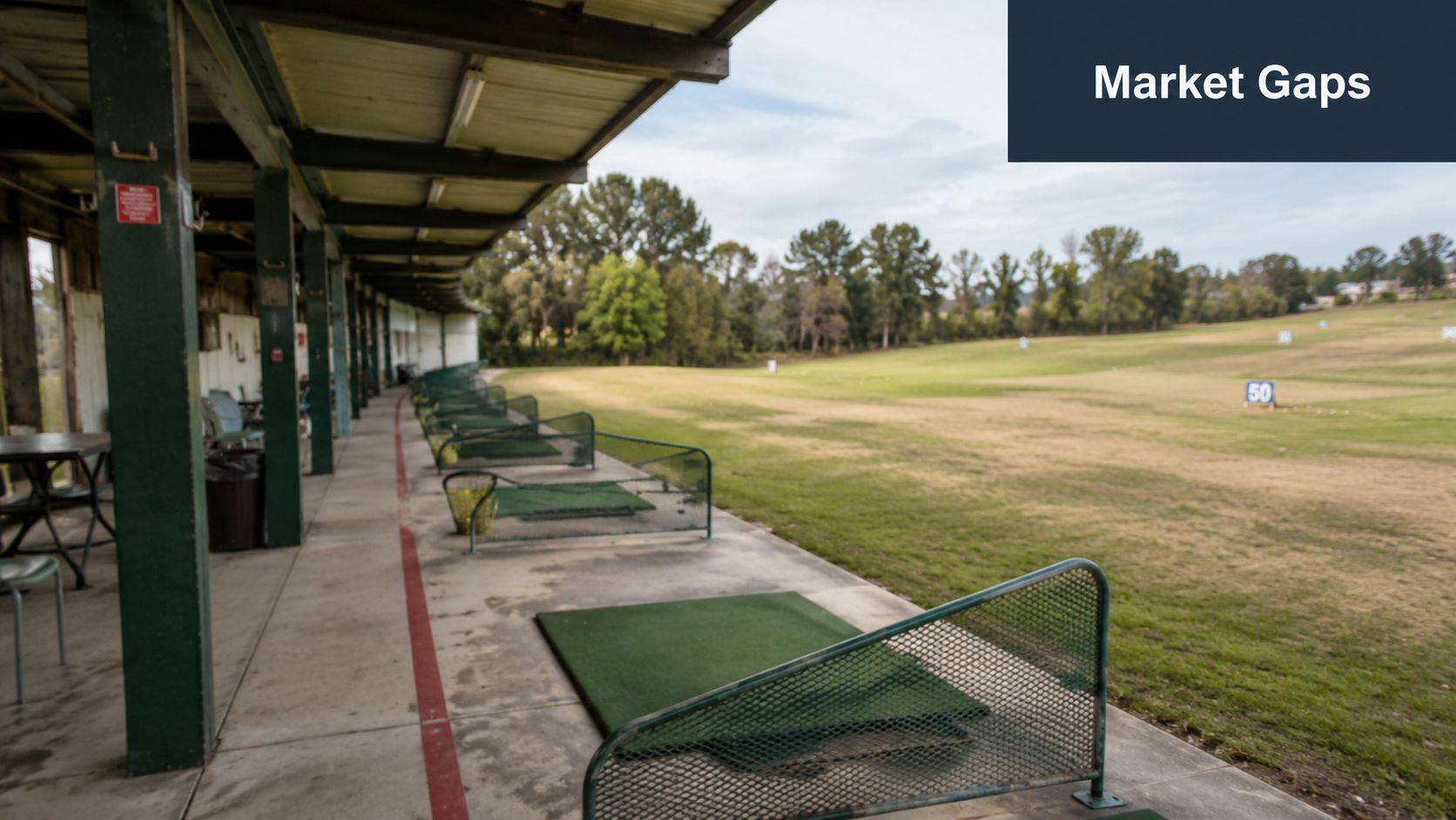 An empty outdoor driving range with golf practice mats and dividers under a covered concrete structure.