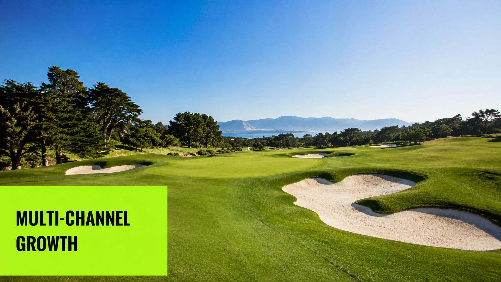 A picturesque view of a lush green golf course with bunkers and mountains in the distance.