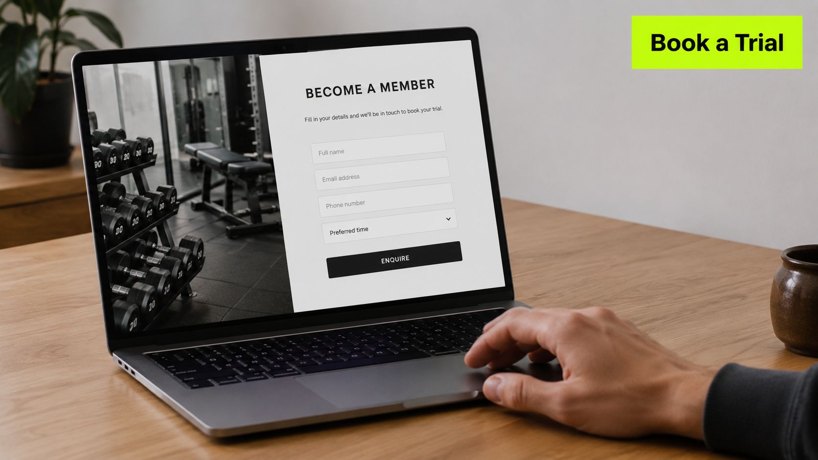 A person using a laptop on a wooden desk to fill out a gym membership trial form.