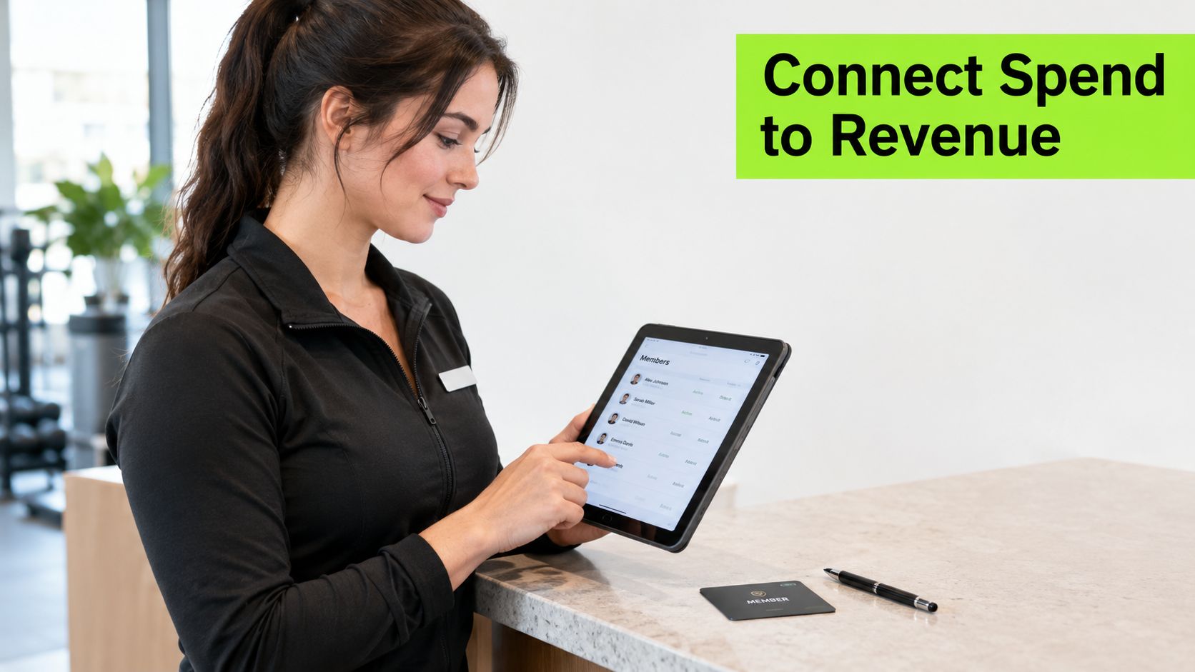 A professional gym staff member using a tablet to manage member data at a modern reception desk.