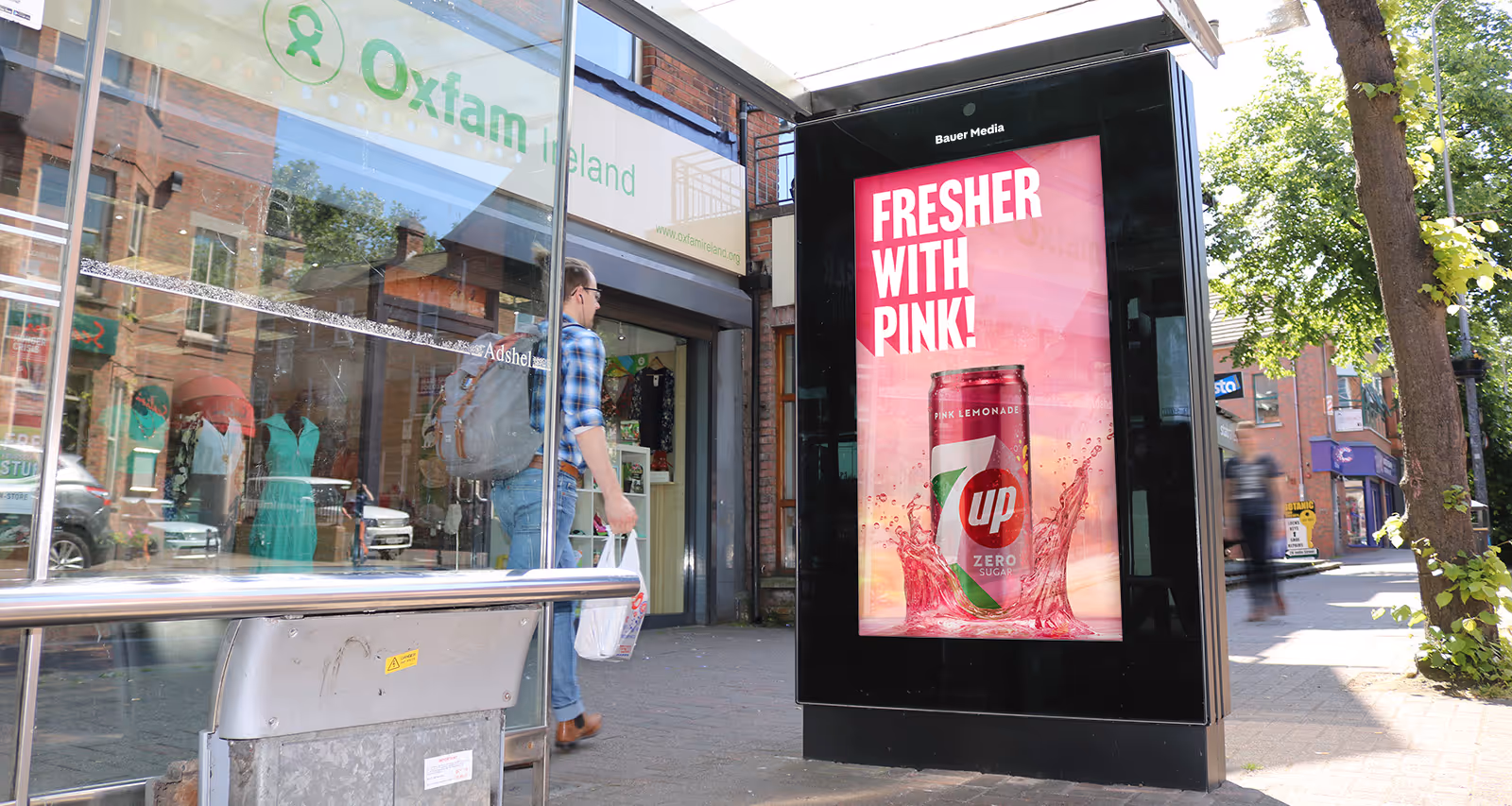 A digital bus shelter advertisement on a busy shopping street with people walking by 