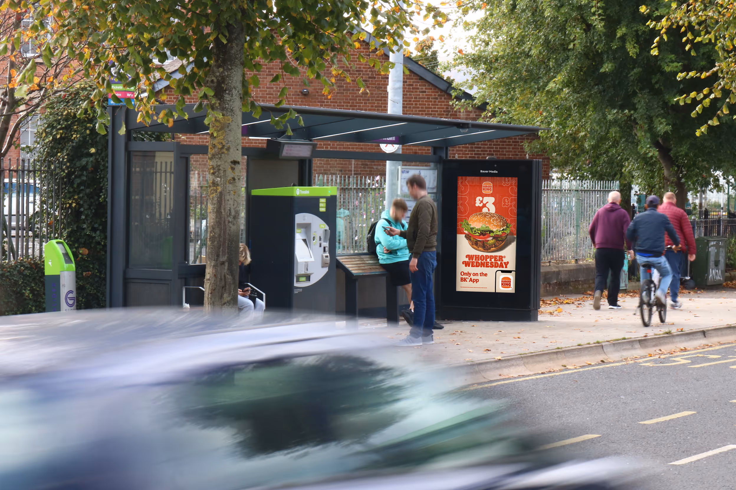 A digital bus shelter advertisement on a busy shopping street with people walking by 
