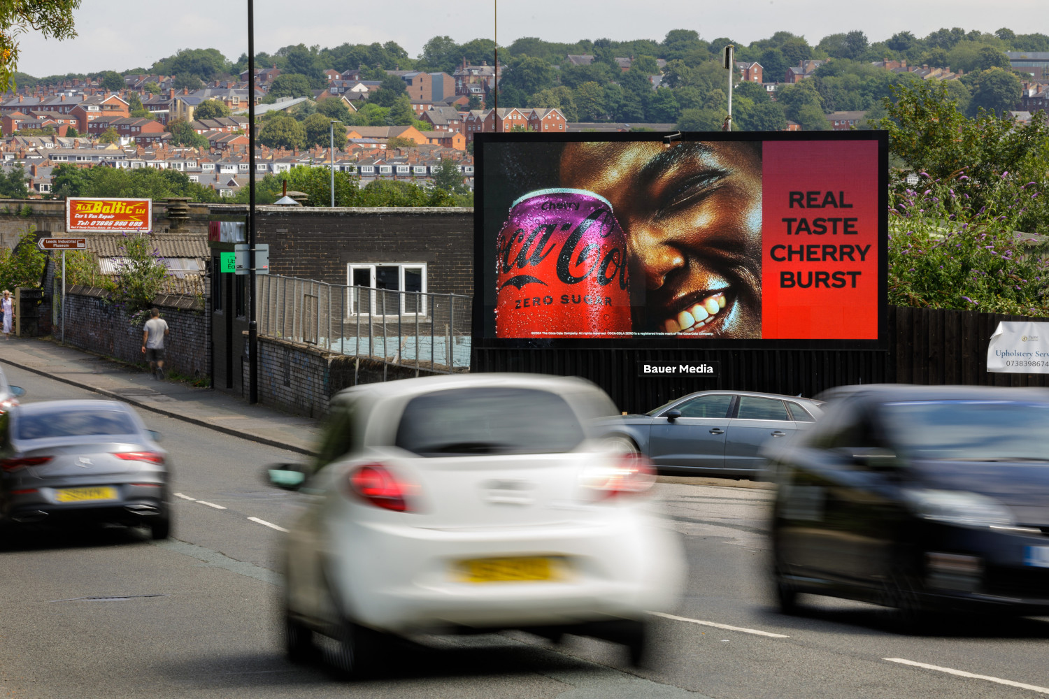 Vehicles driving past a Coca Cola billboard advert