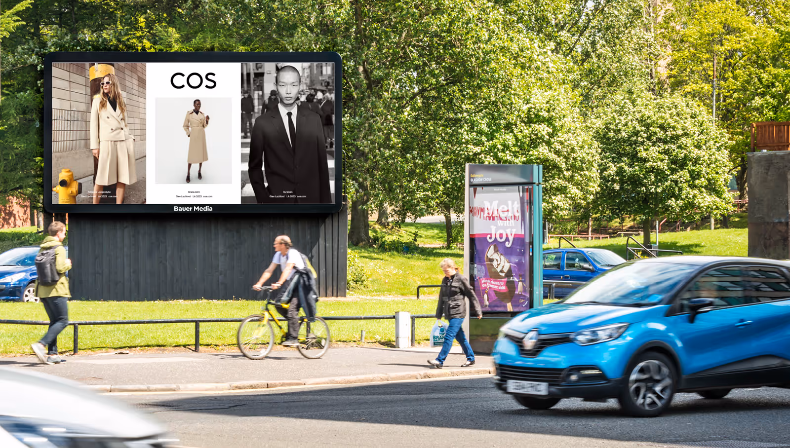 A COS advert is displayed on a billboard by a busy road, during the day, as pedestrians and cars pass by