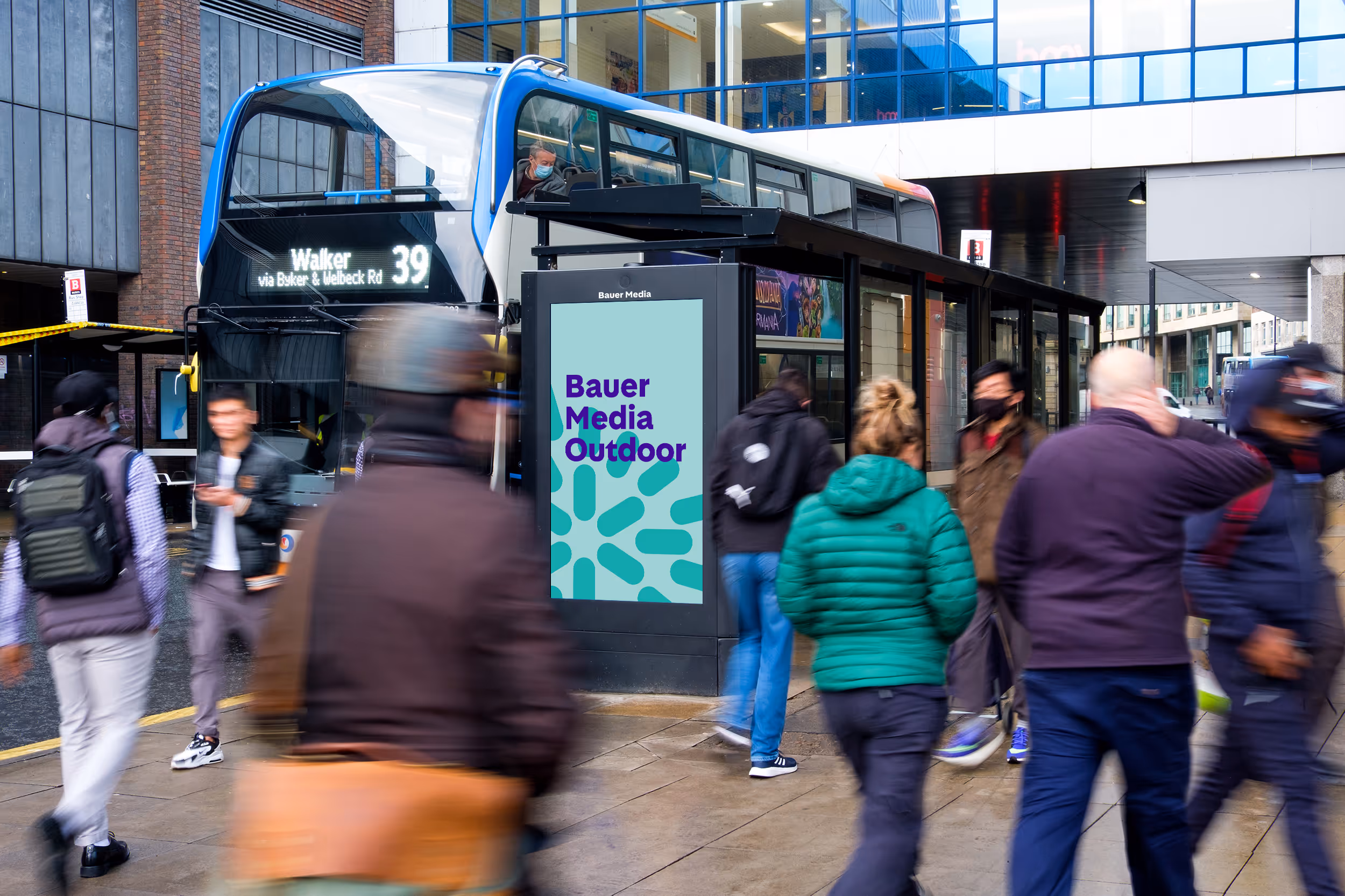 Bauer Media Outdoor advert features on the side of a bus shelter as a bus and pedestrians pass by