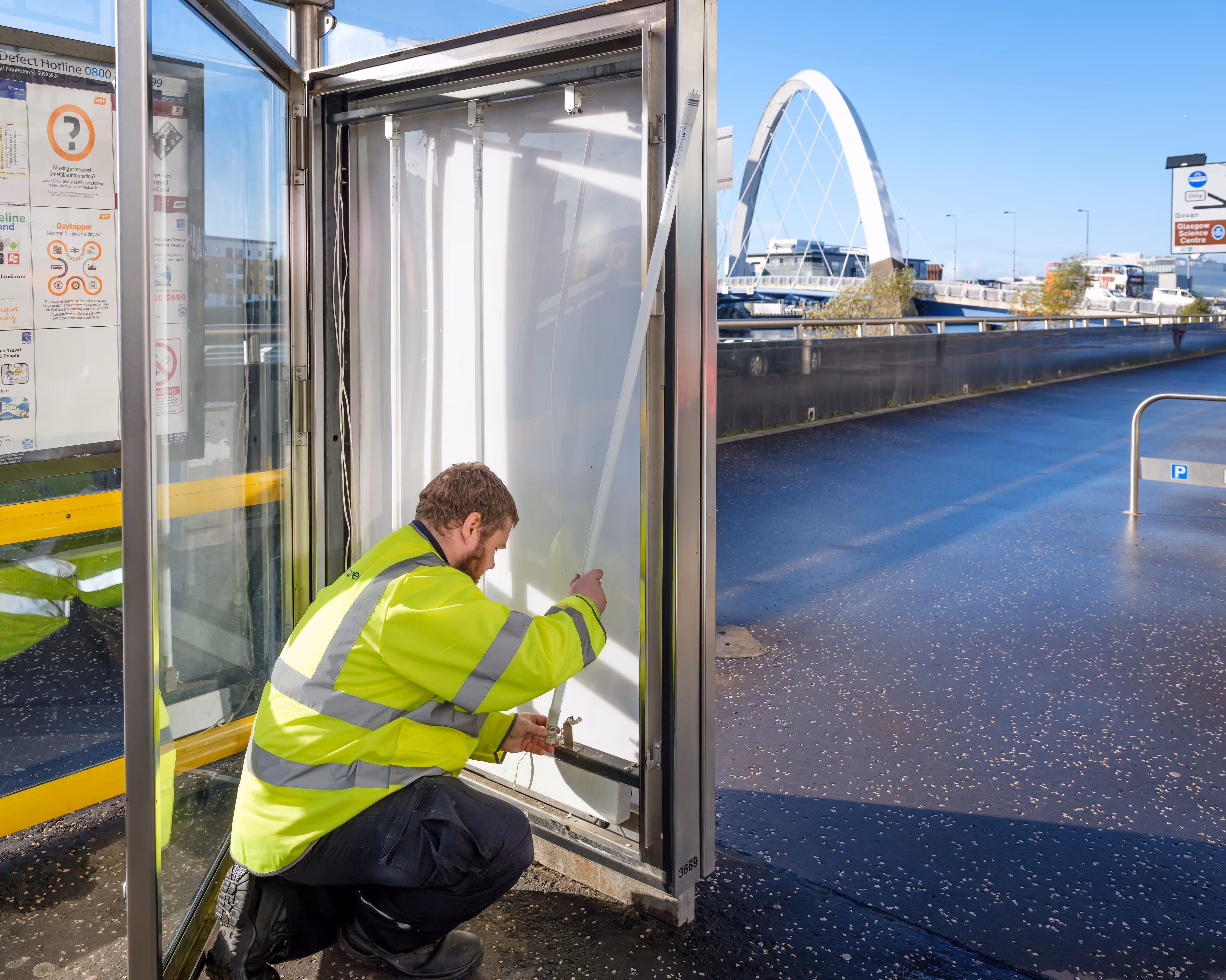 A Bauer Media Outdoor operative replaces lighting at a bus shelter during the day