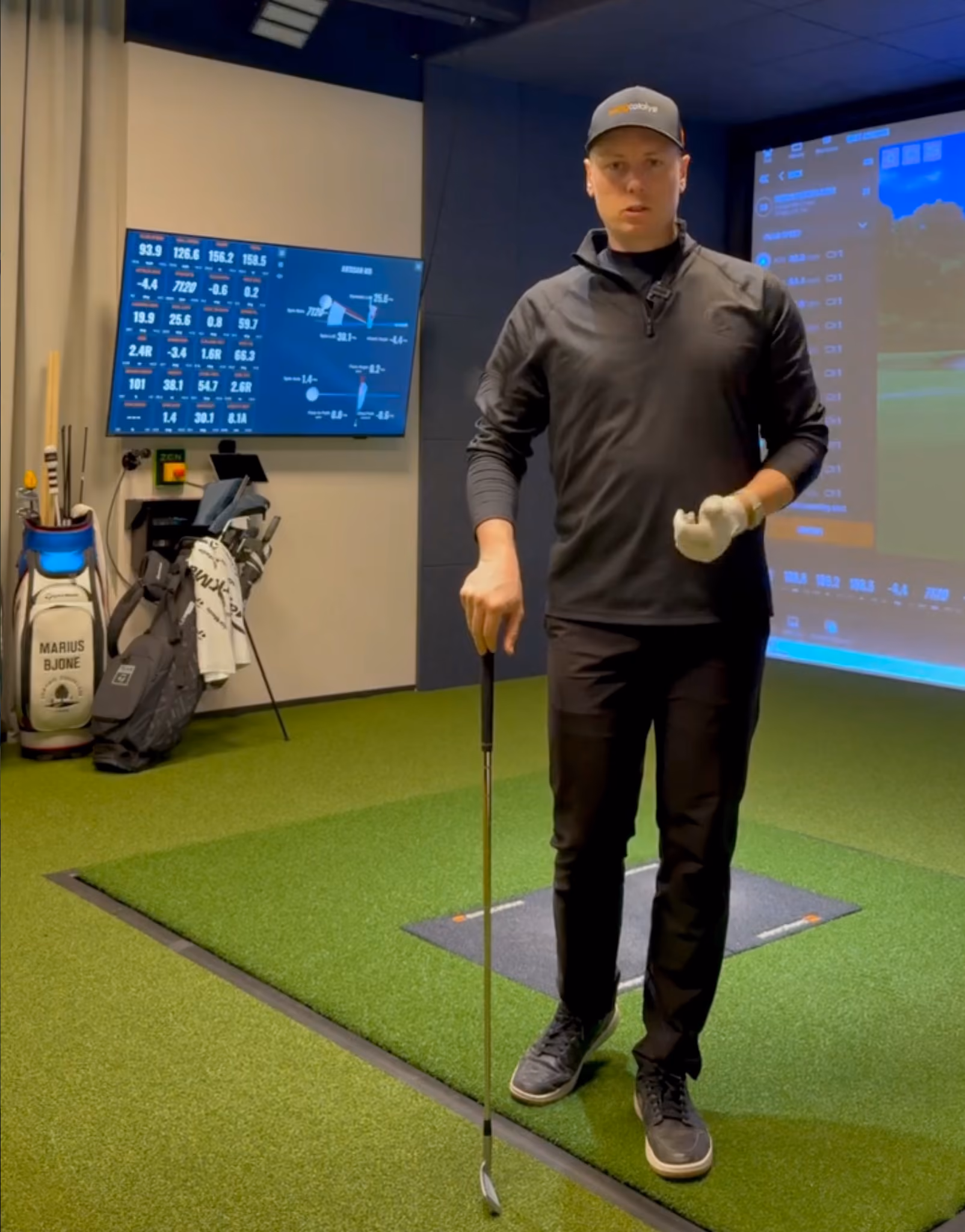 Golftrener med kølle foran TrackMan-simulator og dataskjerm