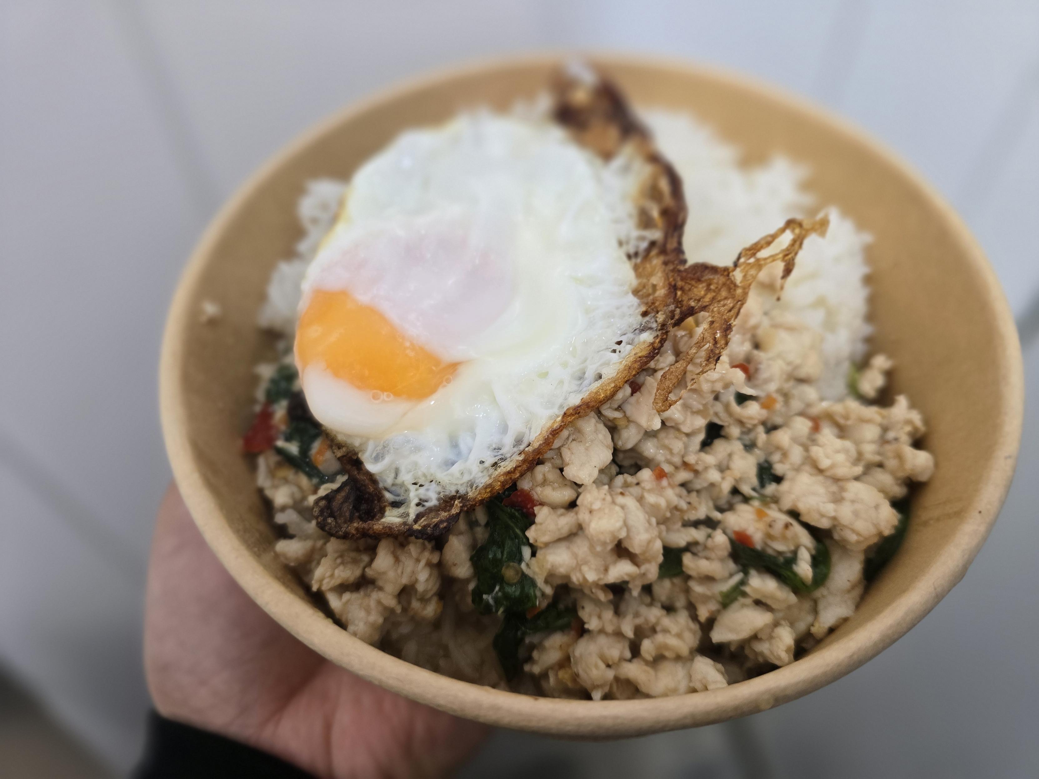 Hand hält eine Schale mit Reis, gewürztem Hackfleisch und einem Spiegelei oben drauf.