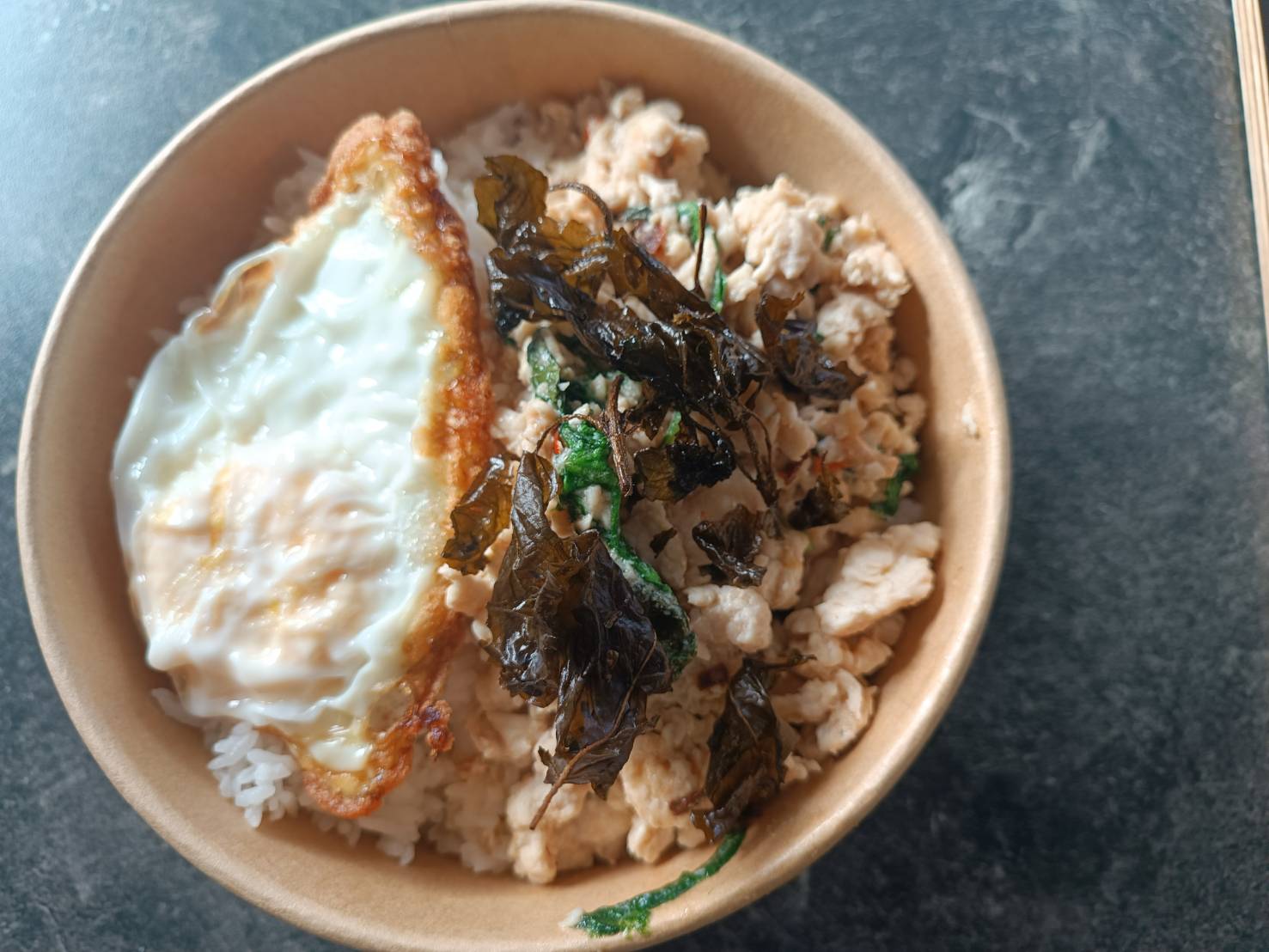 Schale mit Reis, gebratenem Ei, gewürztem Hackfleisch und frittierten Basilikumblättern.