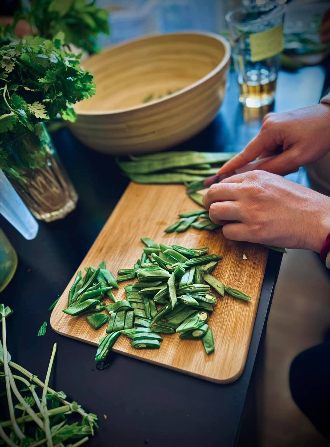 Person schneidet grüne Bohnen auf einem Holzschneidebrett in einer Küche.