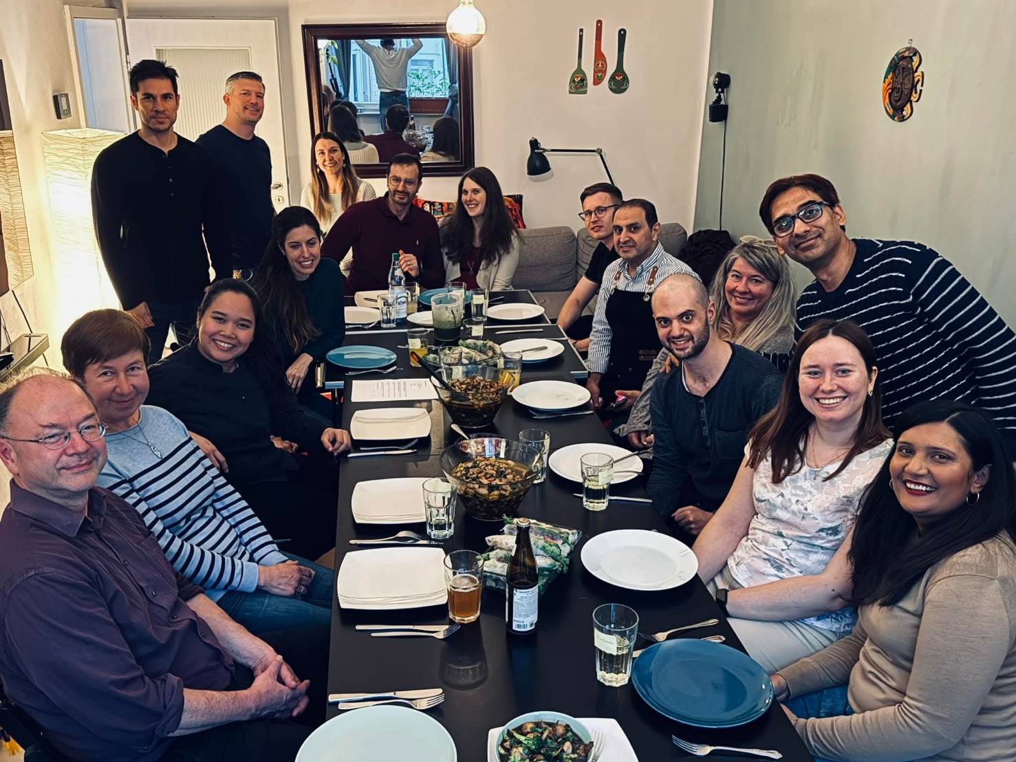 Eine Gruppe von Menschen sitzt fröhlich an einem langen gedeckten Esstisch in einem hellen Raum.