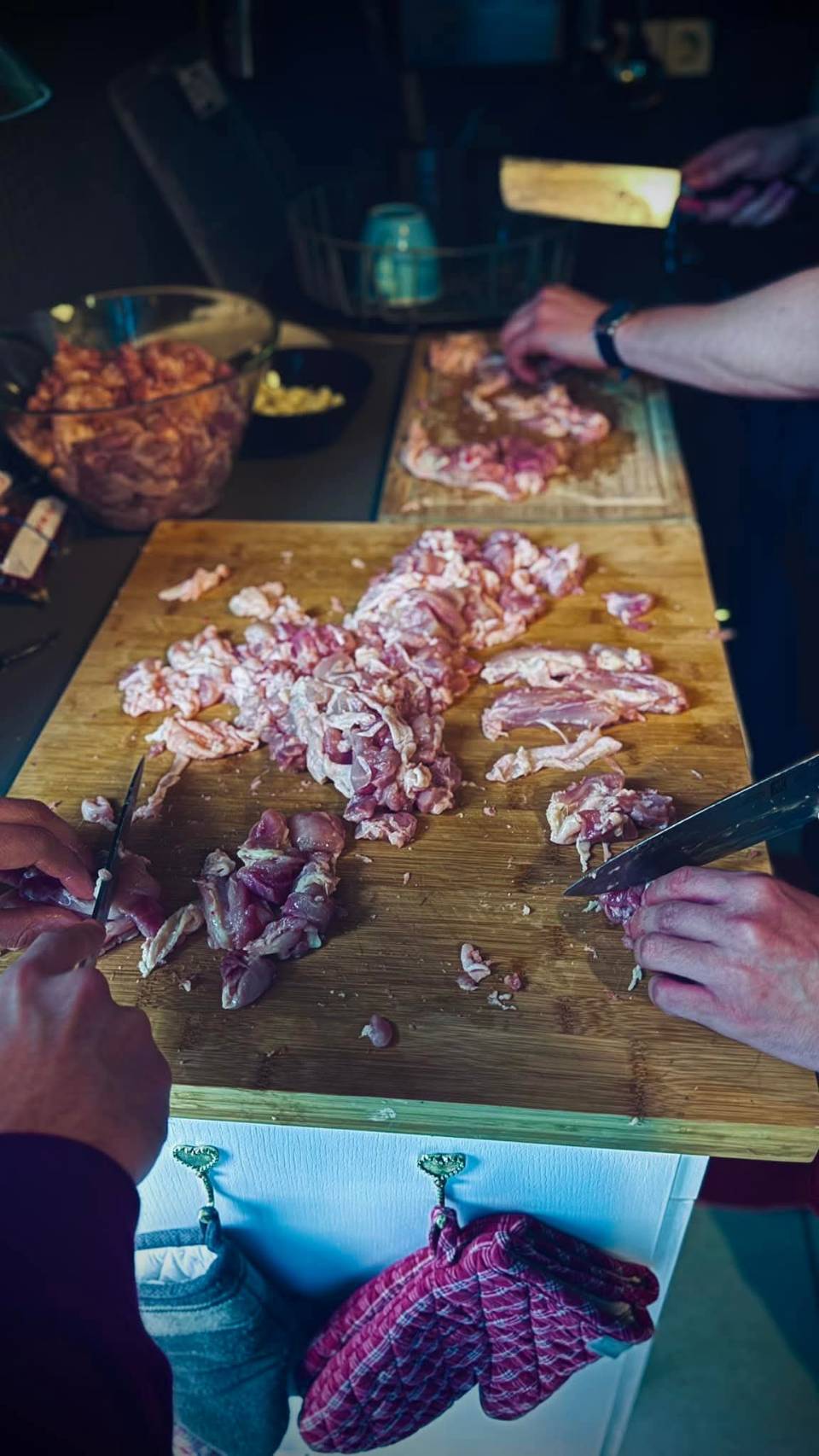 Zwei Personen schneiden rohes Fleisch auf Holzschneidebrettern in einer Küche.