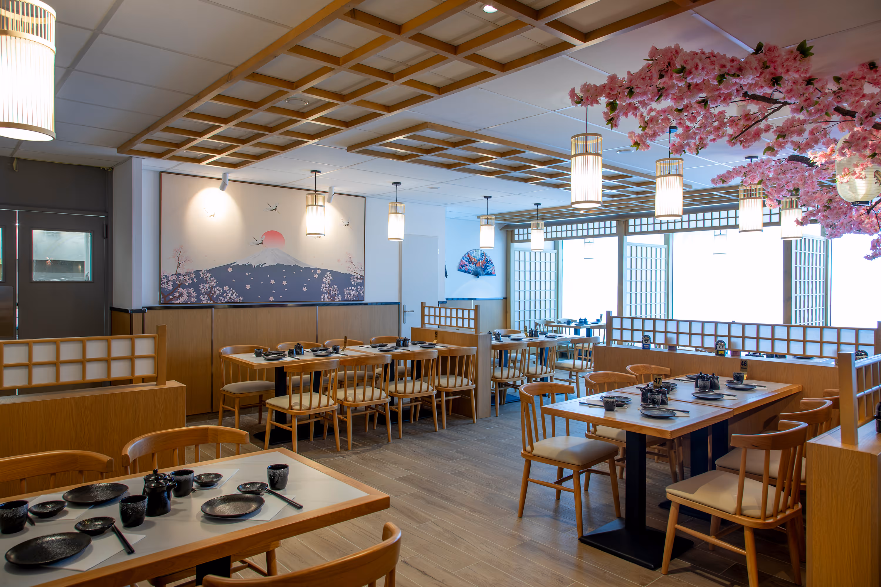 Intérieur d'un restaurant japonais avec tables en bois, décorations traditionnelles et branches de fleurs de cerisier au plafond.