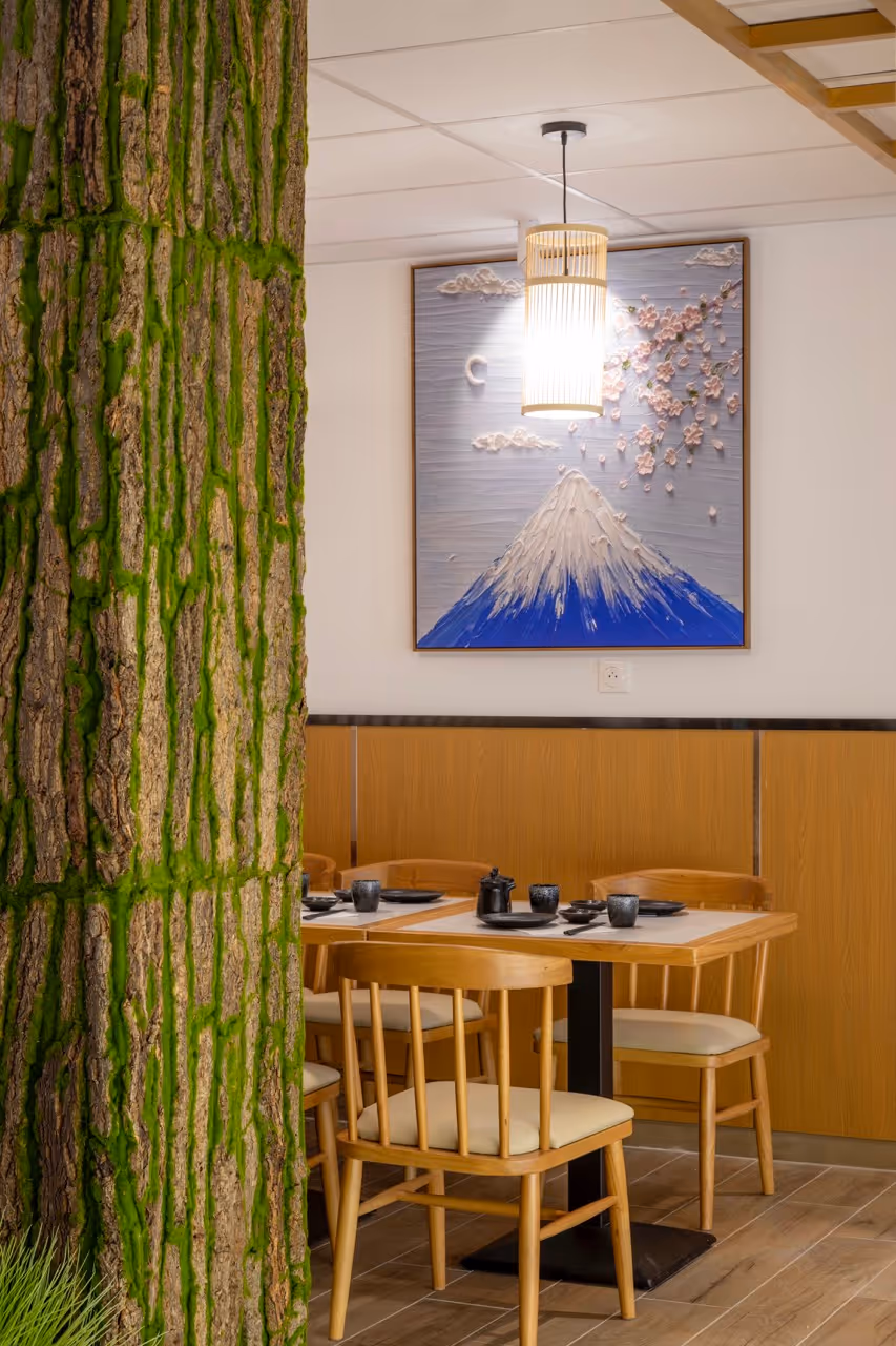 Coin repas avec table en bois, chaises assorties, tableau mural représentant le mont Fuji et une suspension lumineuse.