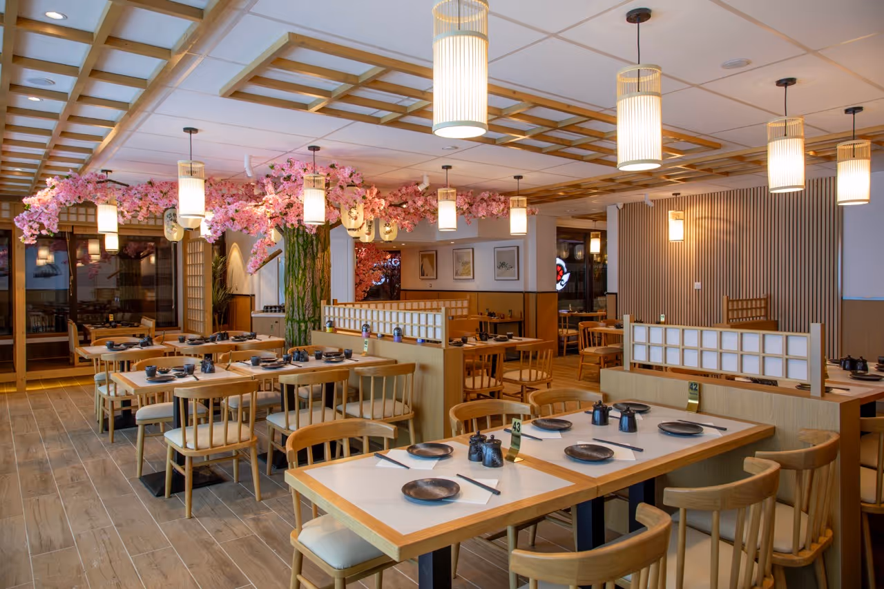 Intérieur d'un restaurant élégant avec des tables en bois clair, des chaises assorties, et une décoration florale suspendue de fleurs roses autour d'un pilier central.