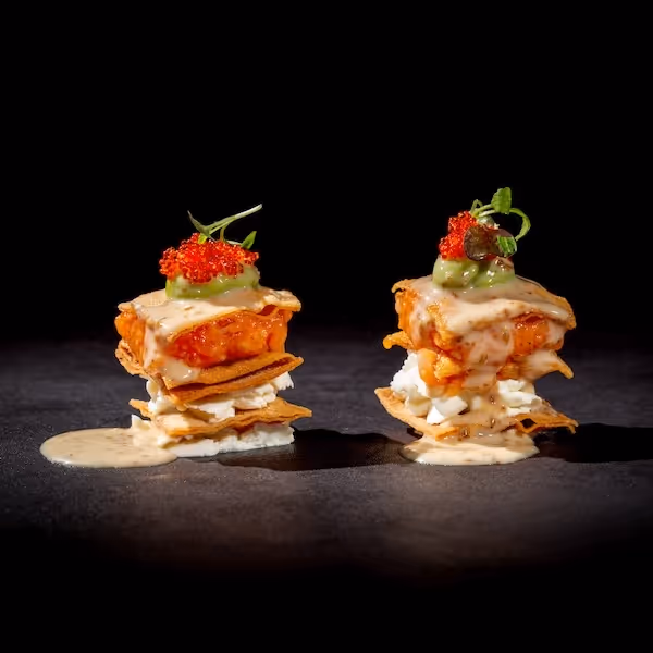 Deux petites tours de chips croustillantes garnies de morceaux de poulet, sauce crémeuse, œufs hachés, guacamole et œufs de poisson rouges sur fond noir.