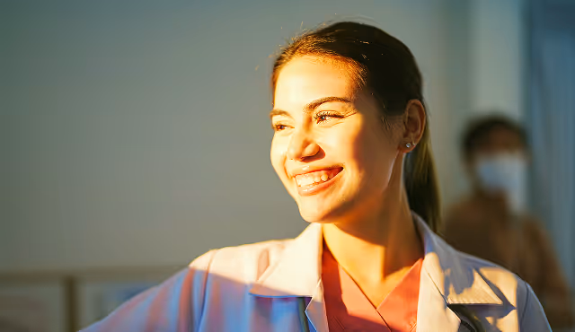 Eine Dame mit einem Kittel, die seitlich zum Sonnenschein guckt und lächelt.