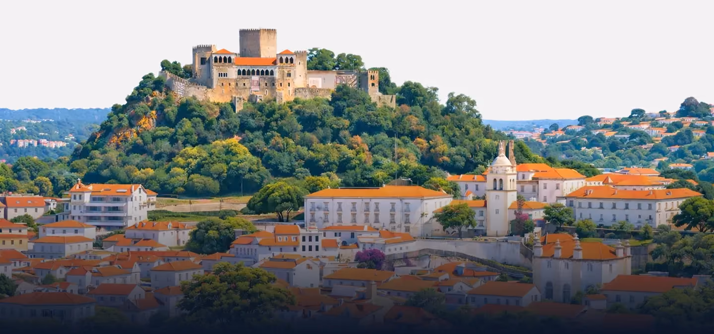 Vista panorâmica de uma cidade vibrante com edifícios de telhados vermelhos rodeados por colinas verdes.