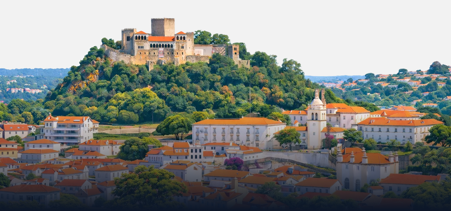 Vista panorâmica de uma cidade vibrante com edifícios de telhados vermelhos, rodeada por colinas verdes.