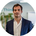 Man with short dark hair and mustache wearing a navy blazer and white shirt in a modern office setting.