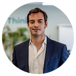 Man in white shirt and navy blazer standing indoors with blurred office background.