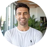 Smiling man in a white shirt standing indoors with blurred background.