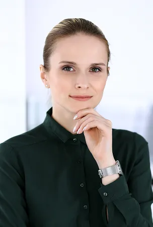Professional woman with light makeup and a ponytail wearing a dark green buttoned-up shirt, resting her chin on her hand.