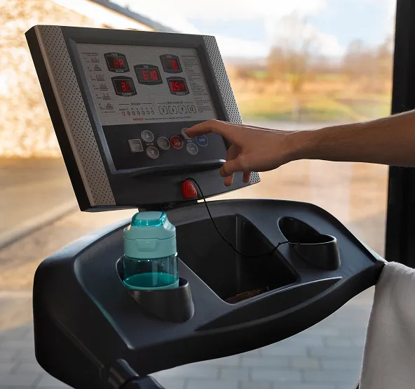 Person pressing a button on a treadmill control panel with a water bottle placed in a holder.
