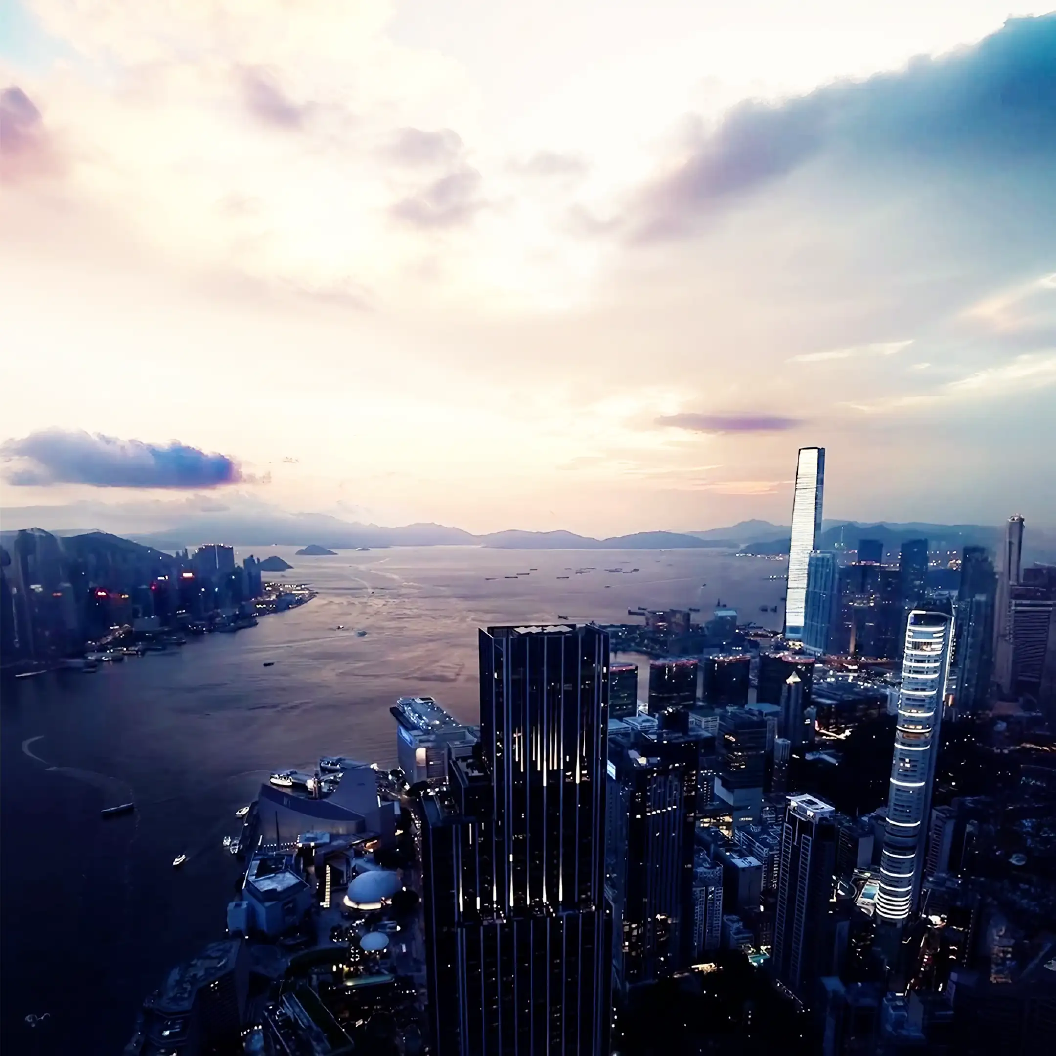 Aerial view of a modern city skyline with tall skyscrapers beside a large body of water during dusk.