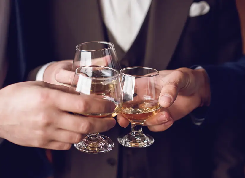 Three people in formal attire clinking glasses of whiskey in a toast.