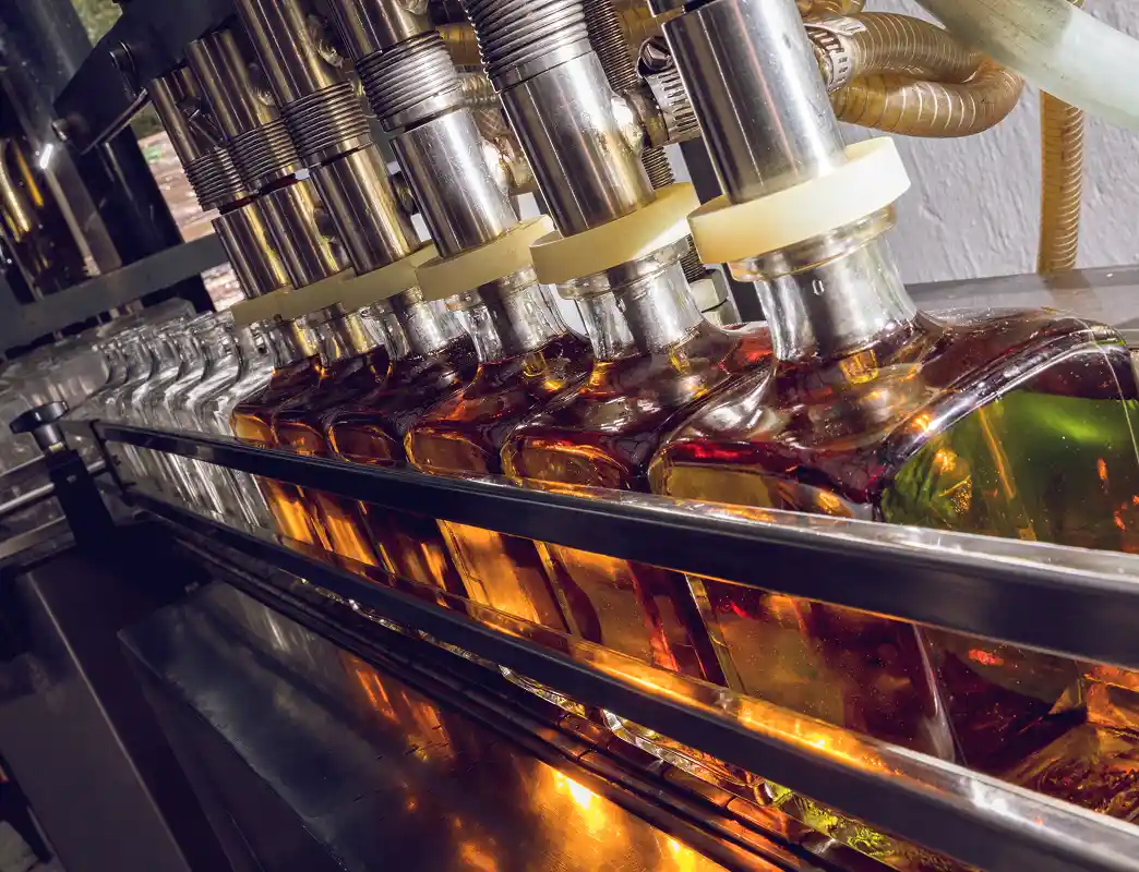 Automated production line filling glass bottles with amber liquid.