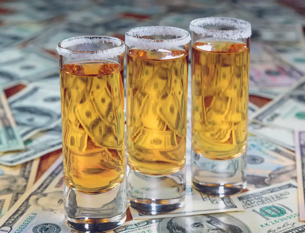 Three tequila shots with salt rims on a surface covered in US dollar bills.