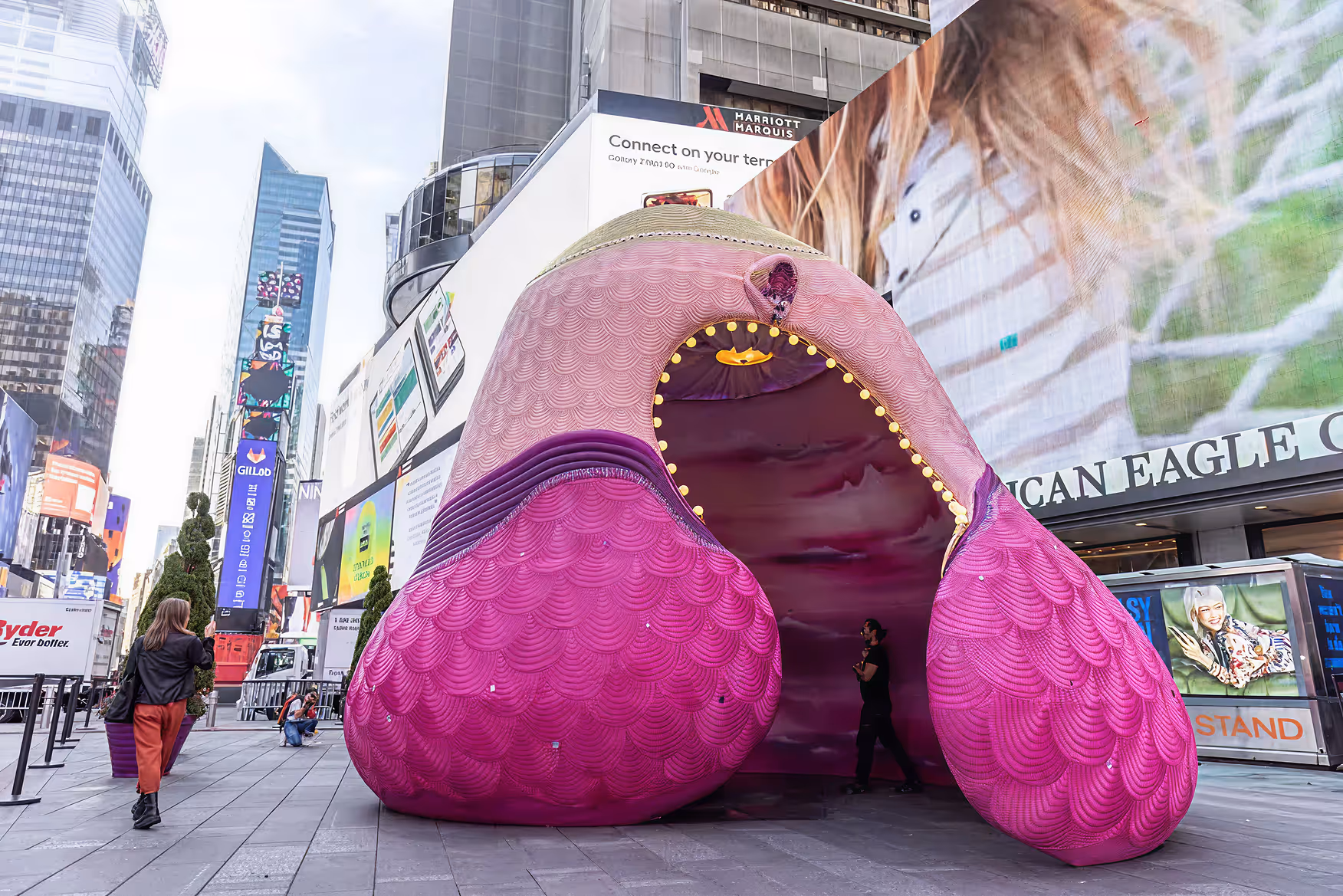 Large pink and purple sculptural art installation shaped like abstract lips in an urban plaza with people walking nearby.