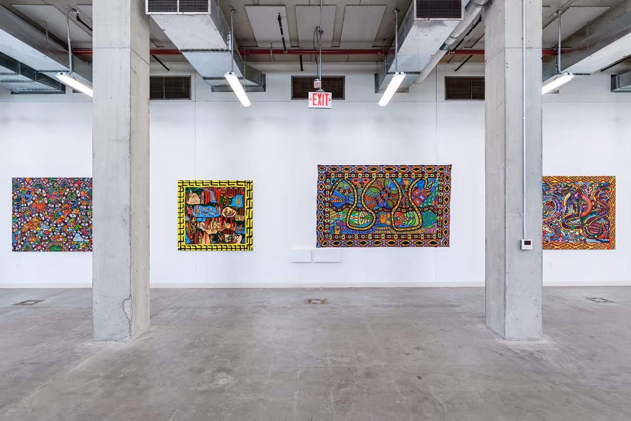 Art gallery interior with four colorful abstract paintings mounted on a white wall between concrete pillars and overhead industrial lighting.