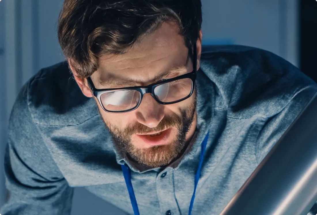 Man with glasses and beard wearing a blue shirt, looking down intently.