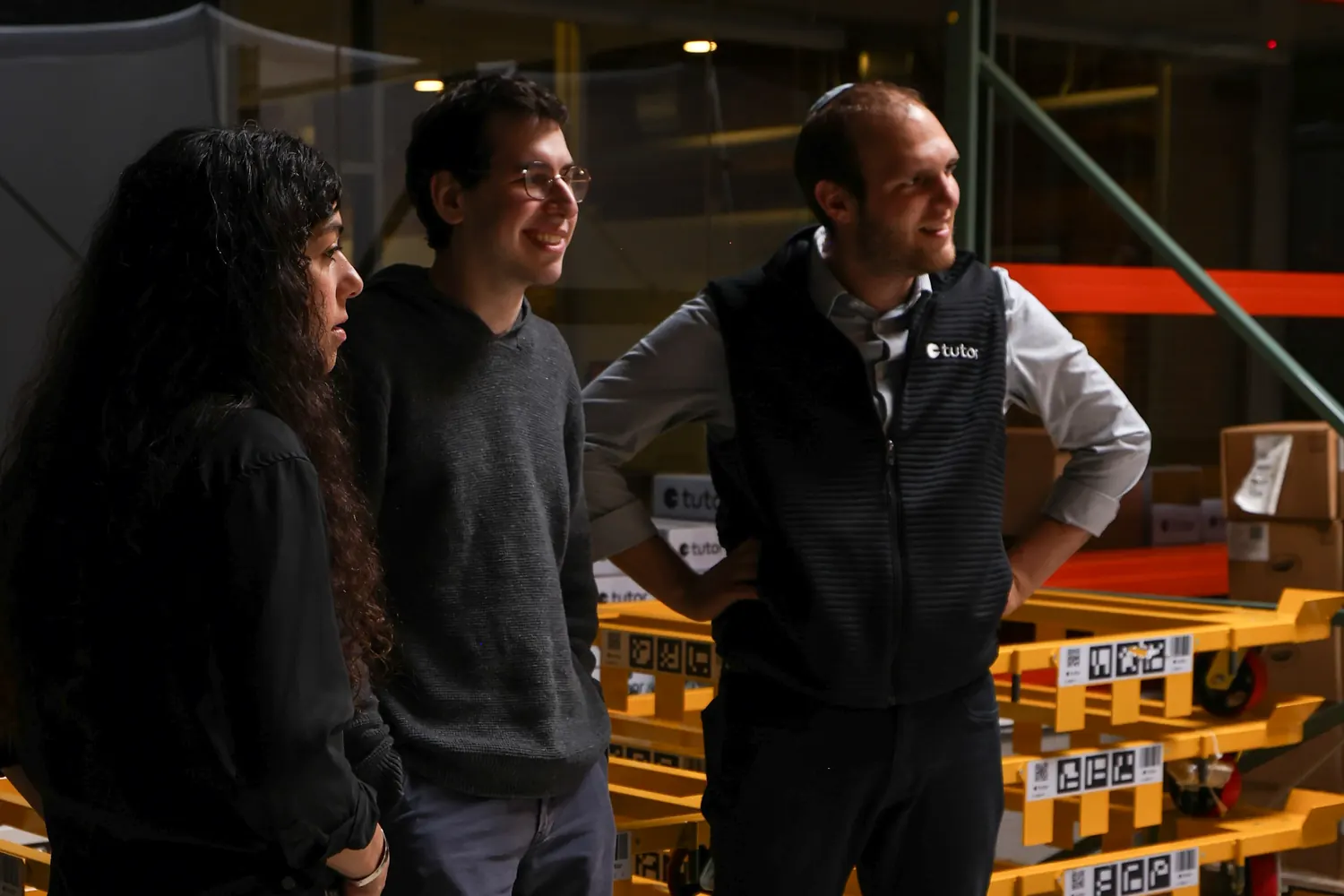 Three people in conversation, in front of stacked Tutor pallet dollies and Tutor branded boxes.