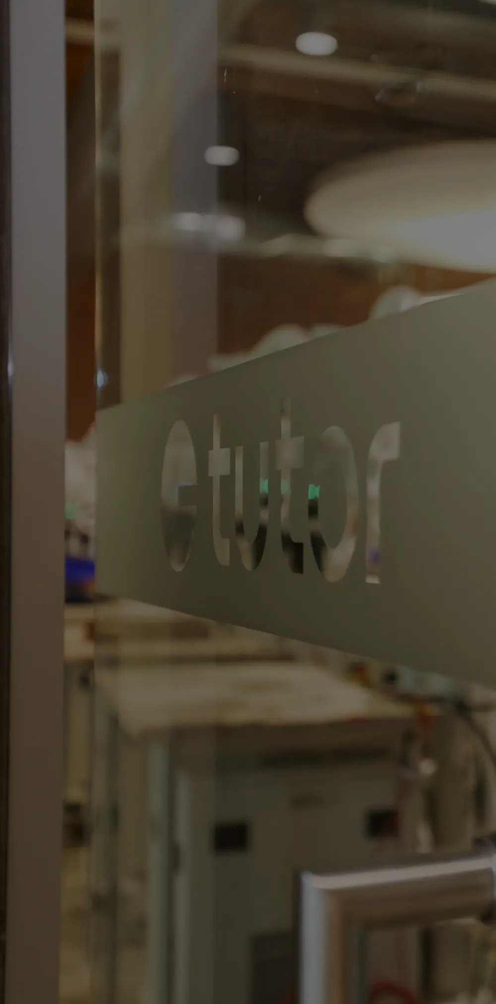 The glass door into Tutor's DF1 robot floor, etched with the Tutor logo, with rows of Sonny robots at work beyond it.