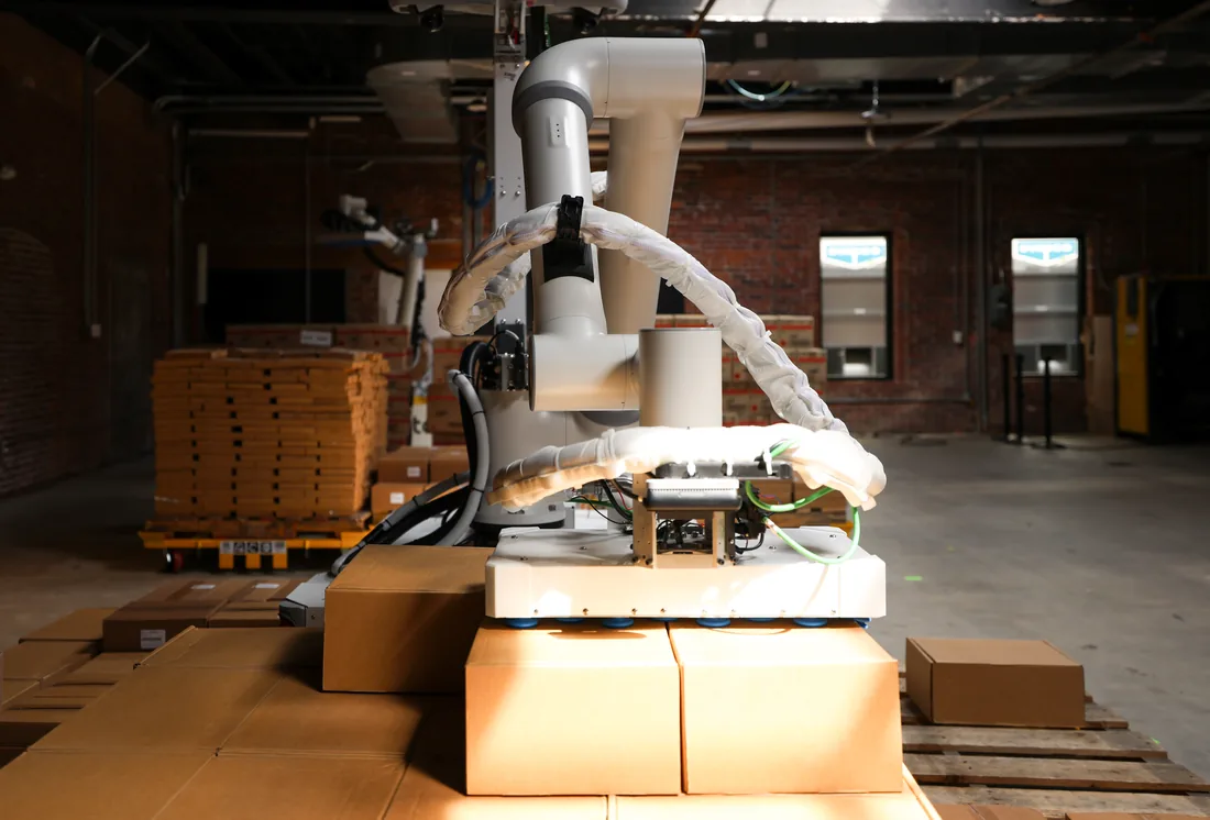 A Tutor Cassie robot arm lowering its suction gripper onto cases stacked on a pallet.