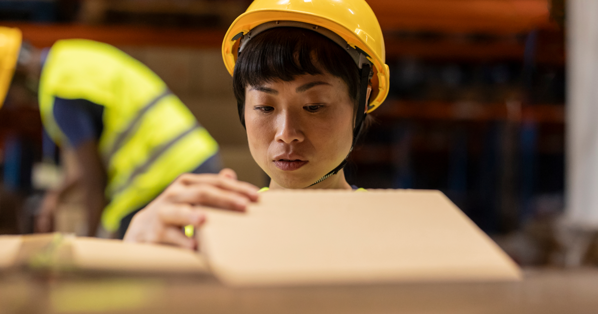 worker in a hard hat inspecting a cardboard box
