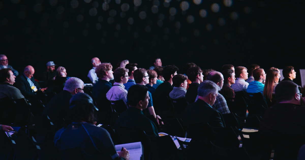 audience seated in rows watching a presentation in a darkened venue