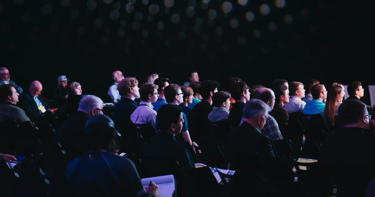 audience seated in rows watching a presentation in a darkened venue