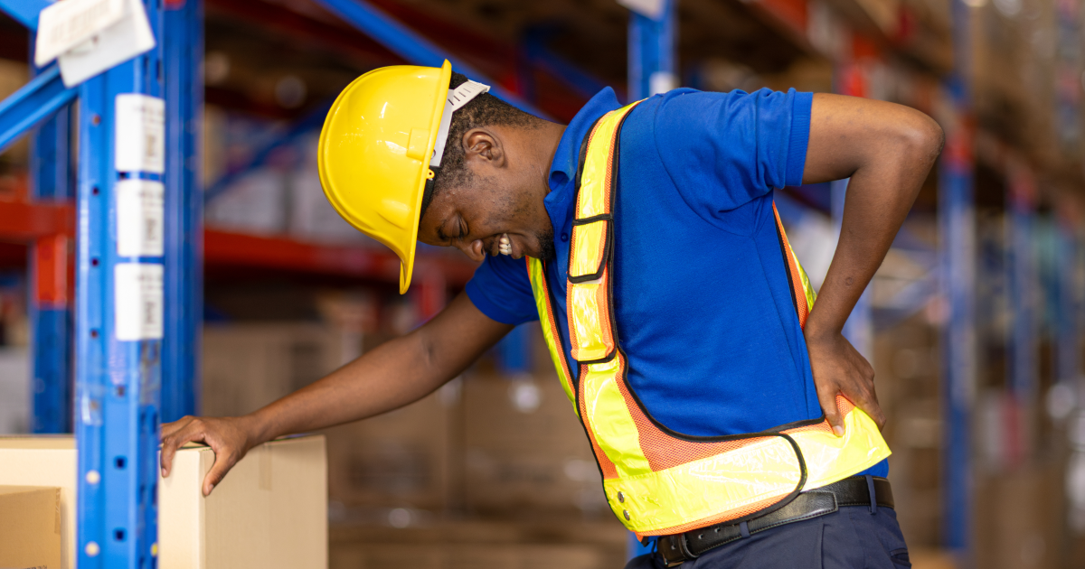 warehouse worker holding his lower back in pain while lifting a box