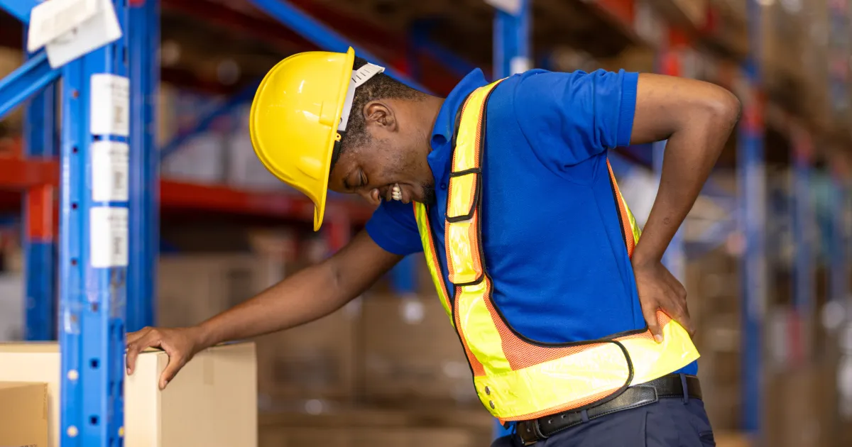 warehouse worker holding his lower back in pain while lifting a box